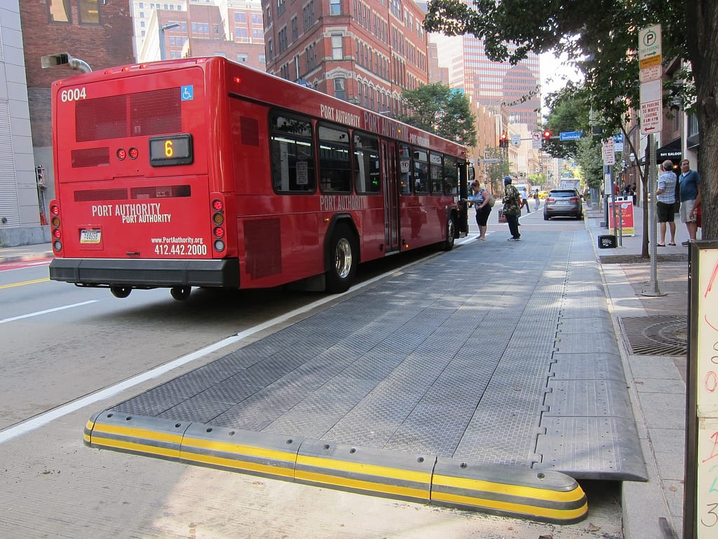 image description: photo of riders using the rubber bus stop extension pads to board a red Port Authority bus from streetsblog.com